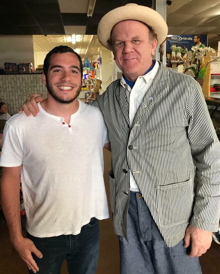 Actor John C. Reilly in a striped jacket and hat, arm-in-arm with a smiling fan during a celebrity encounter.