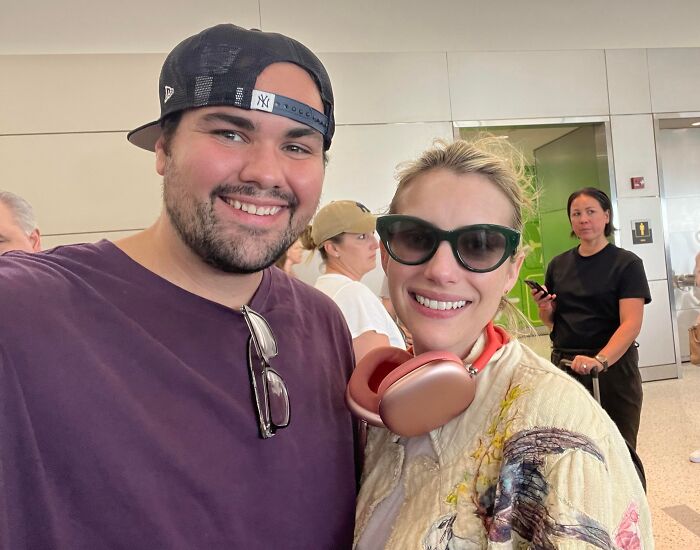 A smiling fan in a Yankees cap posing for a selfie with a celebrity in sunglasses and headphones, capturing a memorable celebrity encounter.