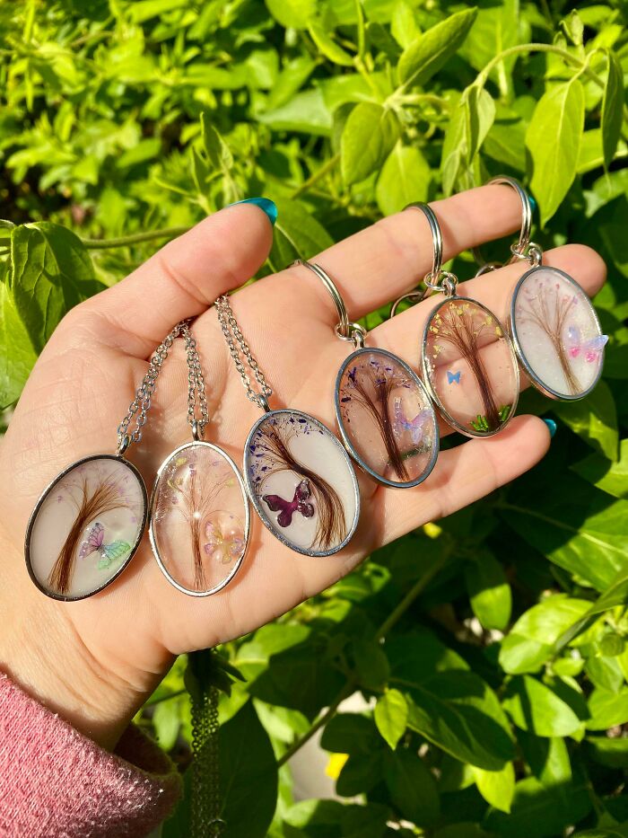 Hand holding multiple handmade resin pendants with encapsulated hair and butterflies, beautiful handmade projects.