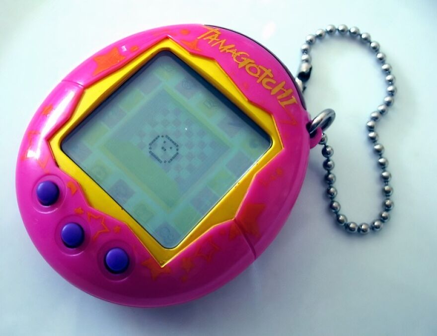 Pink Tamagotchi virtual pet with purple buttons and a metal chain, a nostalgic photo that takes people down memory lane.