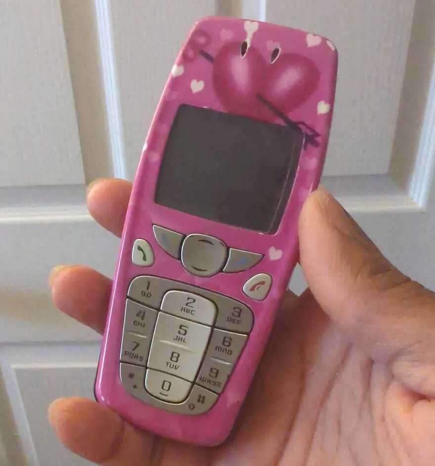 A hand holds a pink flip phone with heart designs, taking people down memory lane to nostalgic tech.