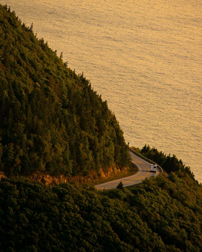 An RV drives along a winding coastal road at sunset, beside a calm, golden sea. A gentle reset moment.