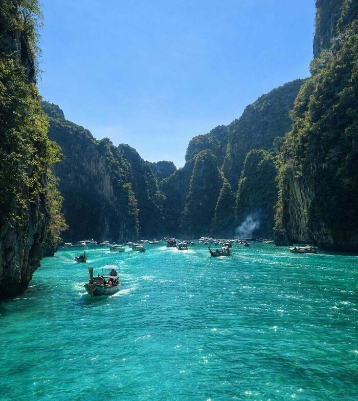 Satisfying pictures of longtail boats on clear turquoise water between lush green cliffs on a sunny day. A gentle reset button for your day.