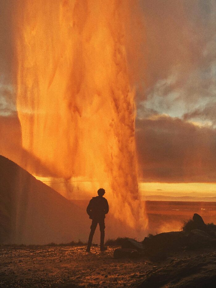 Silhouette of a person admiring a fiery orange waterfall at sunset, offering a gentle reset button for your day.