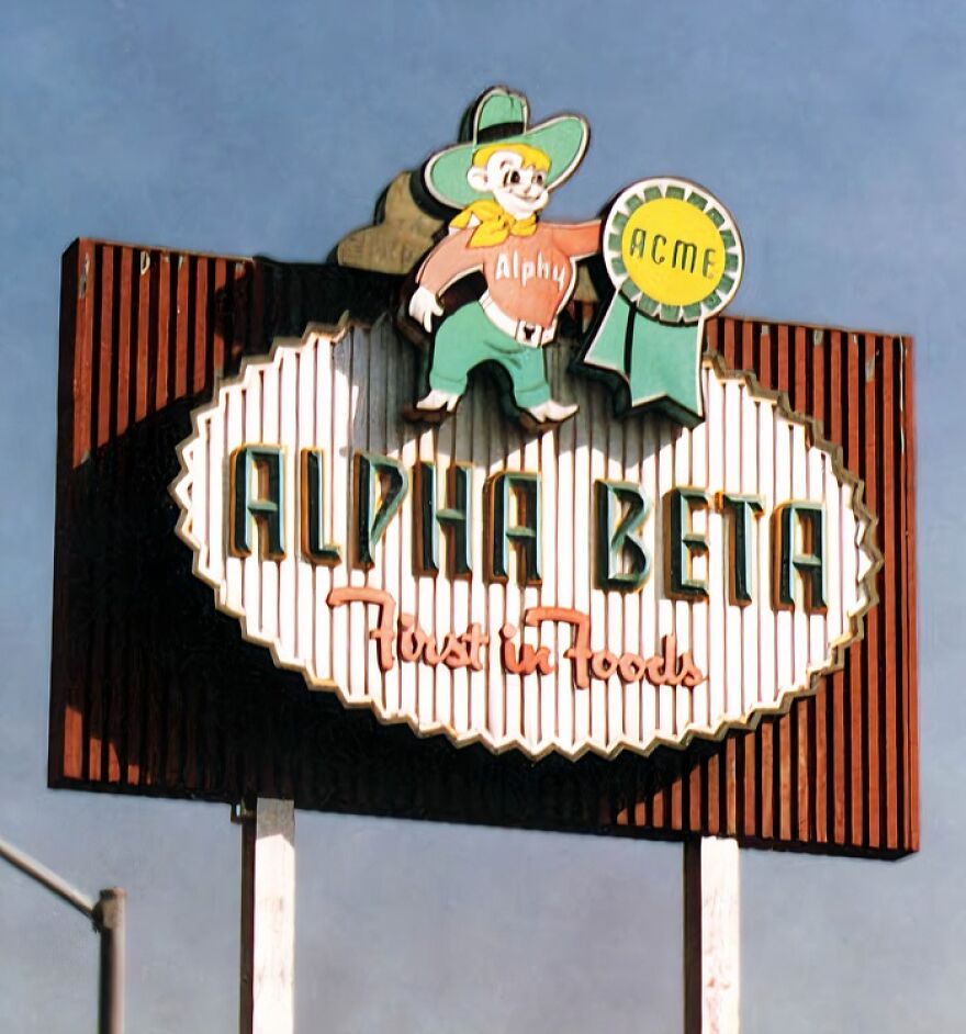 A vintage Alpha Beta sign with a cowboy mascot, Alphy, holding an ACME award, evoking a trip down memory lane.