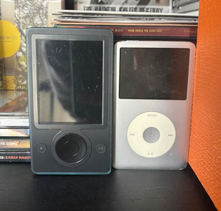Two old MP3 players, a black Zune and a silver iPod, evoking a trip down memory lane for tech enthusiasts.