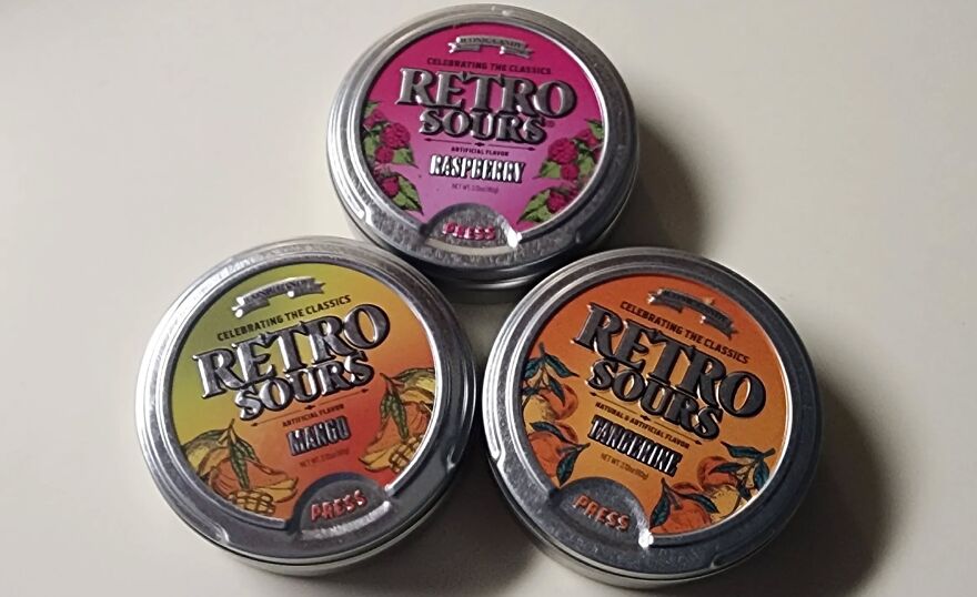 Three tins of Retro Sours candy (Raspberry, Mango, Tangerine) in a triangular arrangement, taking a trip down memory lane.