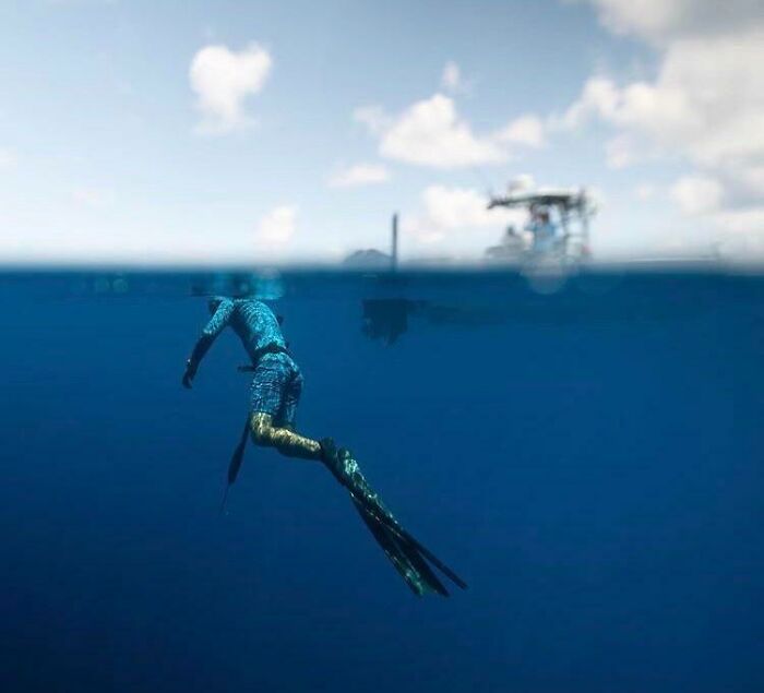 A diver in deep blue water, with a boat visible above the surface, illustrating uncomfortable water pics.