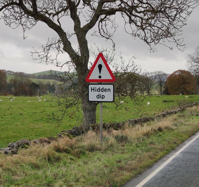 Road sign warning of a hidden dip with countryside background