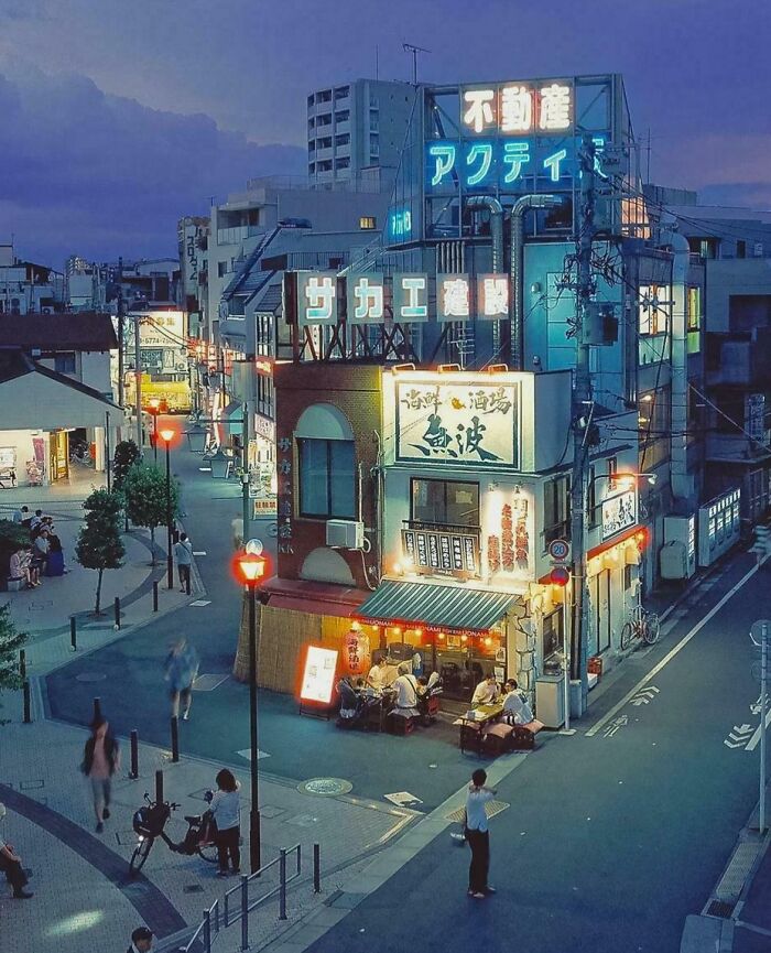 Dusk in a vibrant Japanese street with neon signs and a busy restaurant, showcasing impressive architecture.