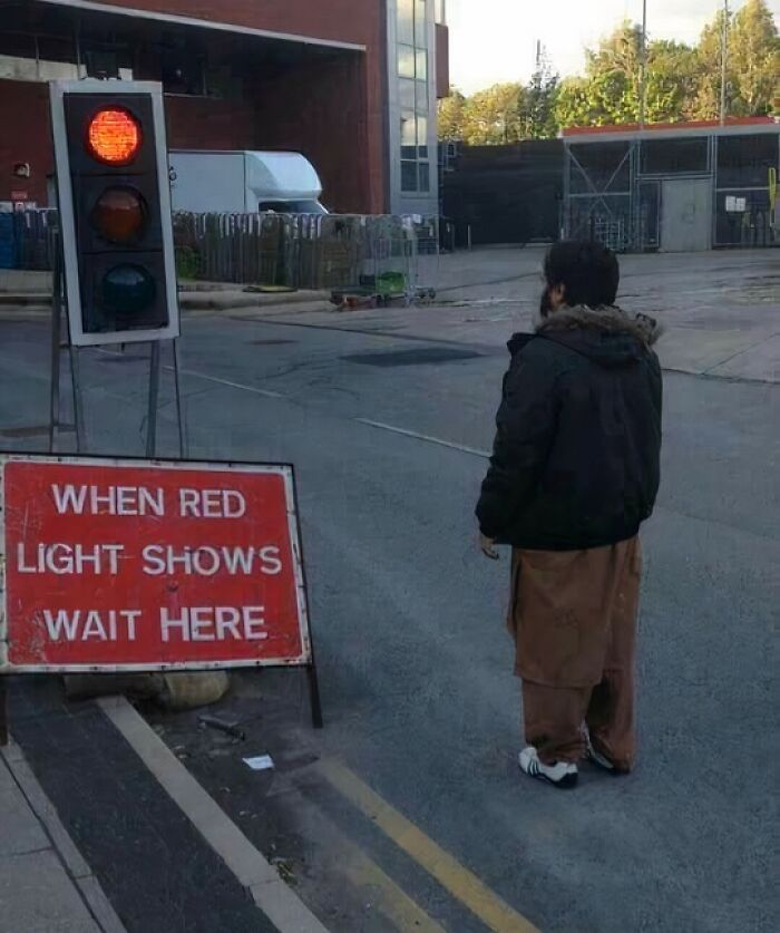 Person standing in front of red traffic light with wait here sign