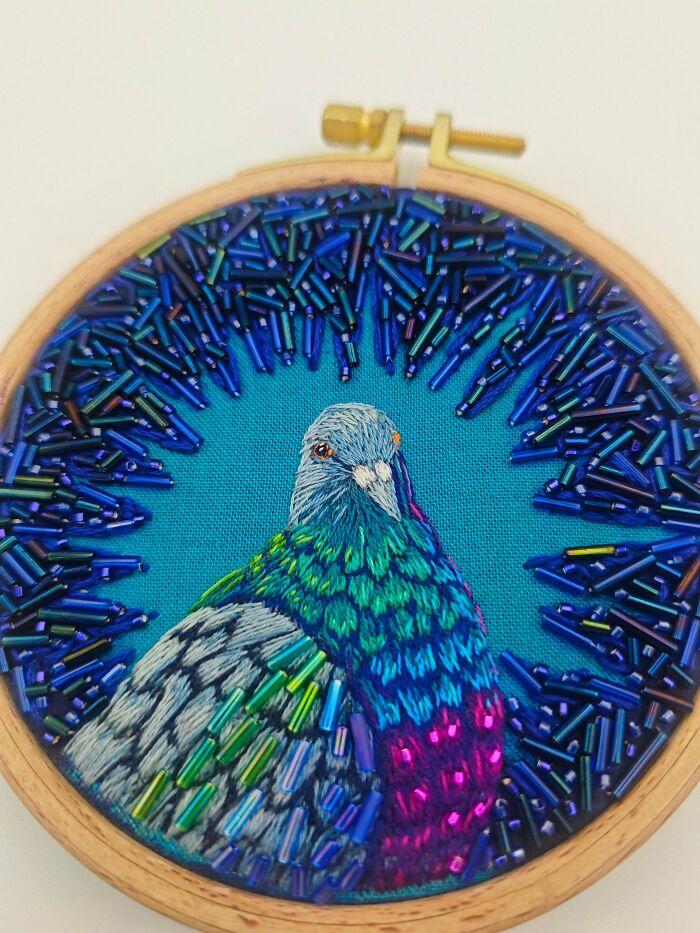 A detailed embroidery project of a pigeon surrounded by blue beaded embellishments
