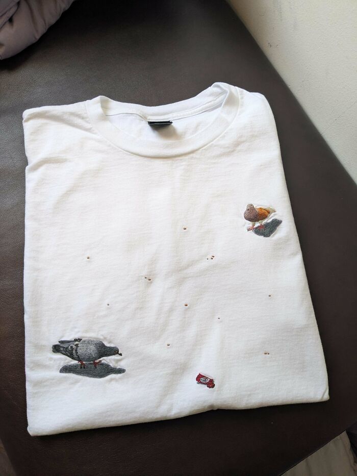 White t-shirt with embroidered pigeons and crumbs, showcasing a unique handmade project with talent.