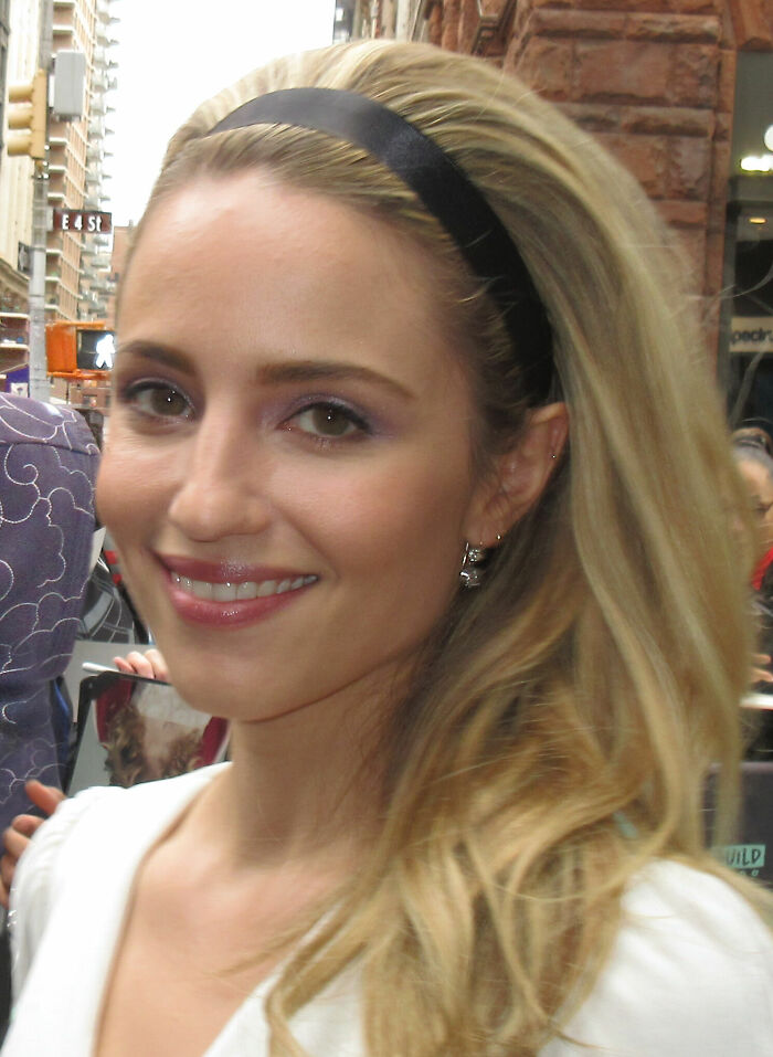 Dianna Agron with a black headband, smiling at a fan event. Her career highlights include acting roles.