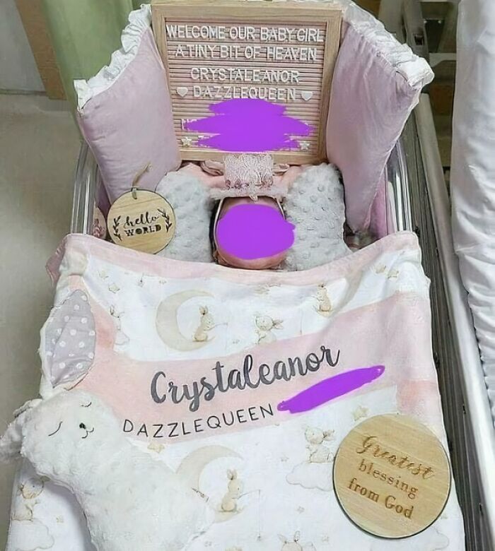 Newborn baby girl in a bassinet with a blanket, sign, and pillow, illustrating parents naming choices.
