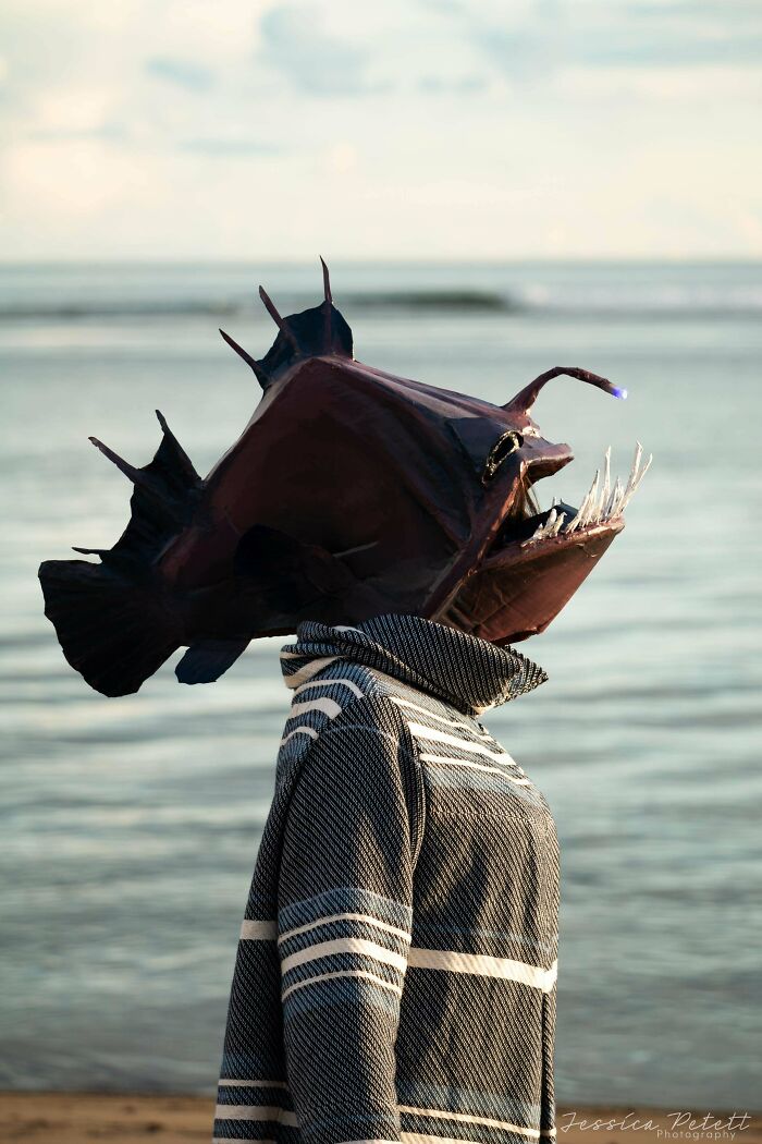 Person in a handmade anglerfish costume with glowing lure, standing by the ocean, a creative handmade project.