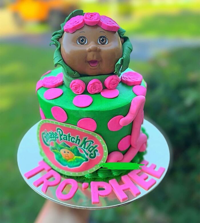 A Cabbage Patch Kids themed birthday cake with a doll head on top, green frosting, and pink polka dots. Parents naming kids.