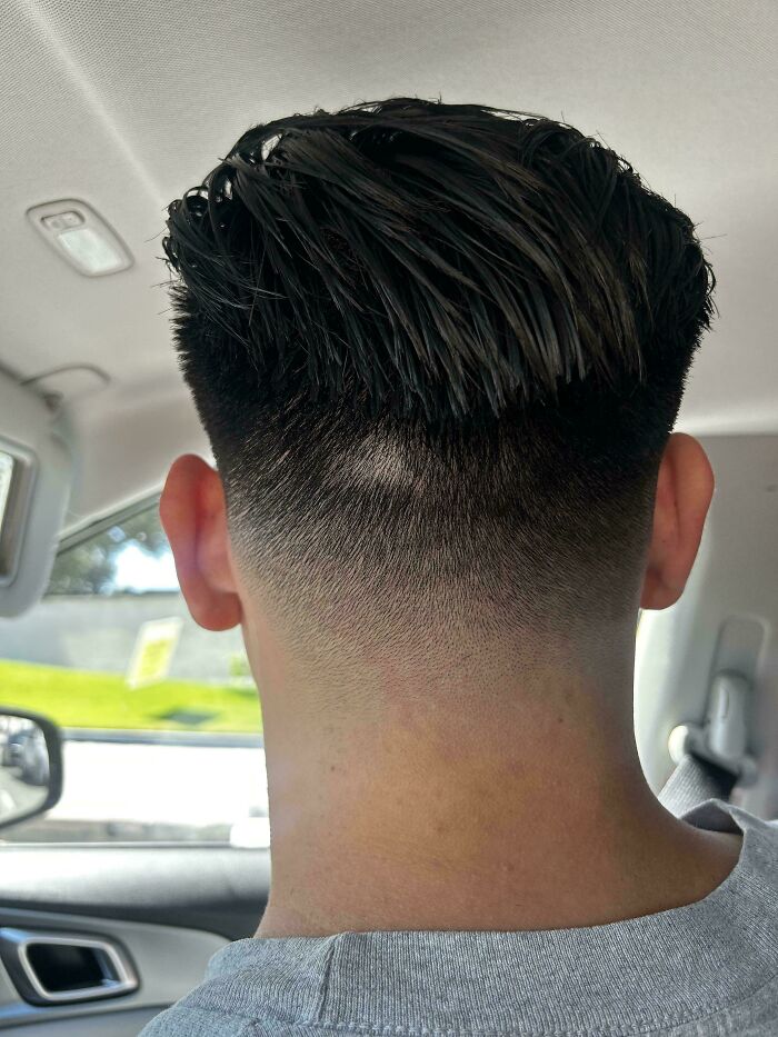 A close-up of the back of a man's head, showing a haircut disaster with uneven fading and a prominent bald spot.