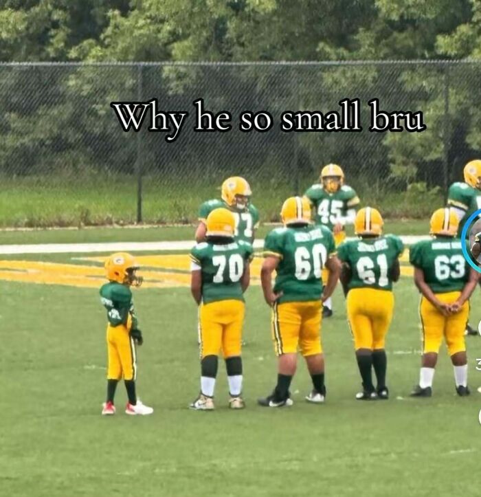 A hilarious, random, unhinged pic of a tiny kid in a football uniform next to larger teammates on a field.