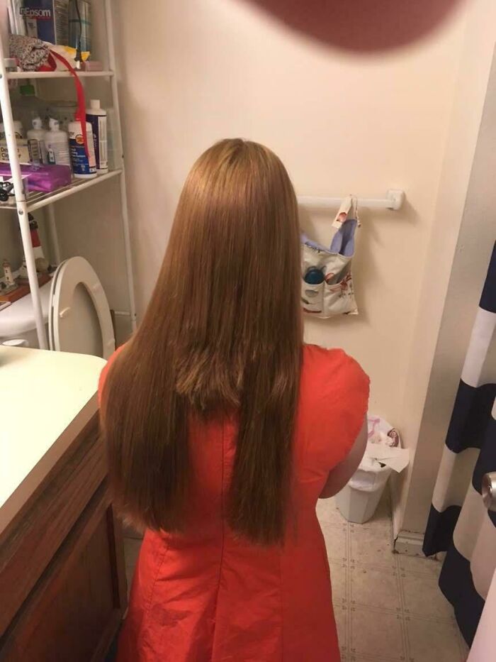A woman with long, light brown hair and an orange dress, facing away, revealing a beauty disaster of uneven layers.