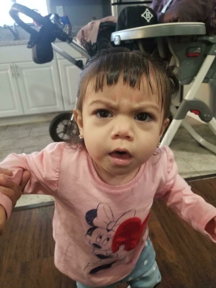 A baby girl with a furrowed brow and short bangs, looking surprised. A beauty disaster with her bangs.