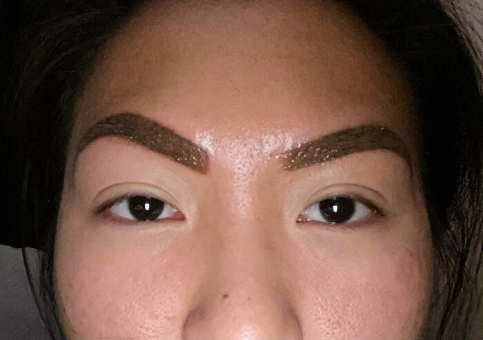 A woman's face with poorly done eyebrows, highlighting a major beauty disaster. Her brows are thick, dark, and uneven.