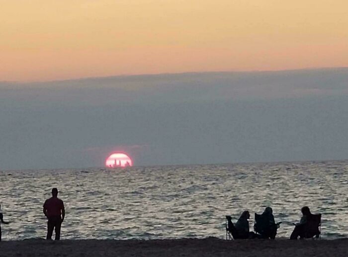 People on a beach watching a sunset over the ocean, an interesting and uplifting post.