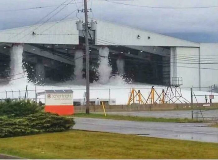 A hangar-like building with large plumes of white foam pouring out, an accident that looks expensive.