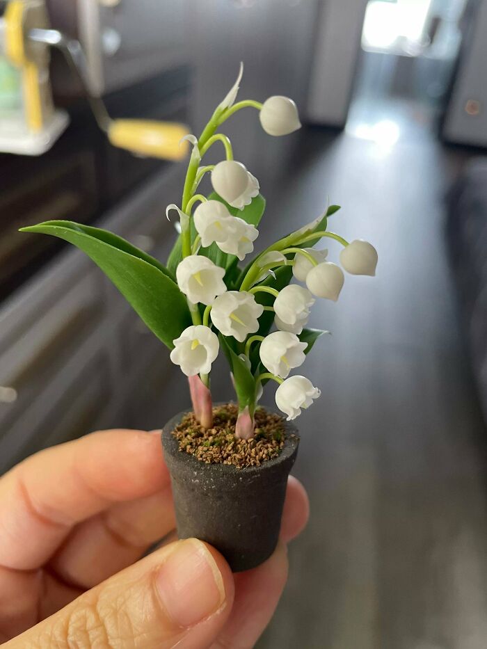 A person holding a tiny, delicate handmade pot with miniature lily of the valley flowers.