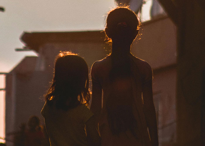 Silhuetas de duas crianças caminhando ao pôr do sol, destacando uma mãe que não acredita nem defende o cenário de seu filho.