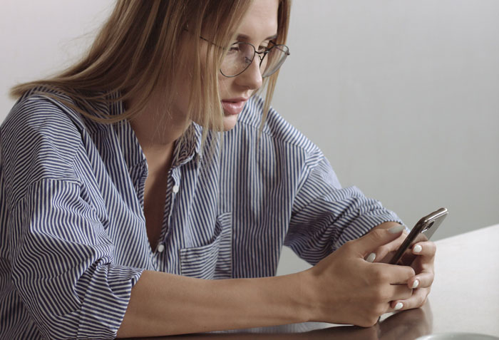 Jovem parecendo surpresa ao ler uma mensagem em seu telefone, reagindo à confirmação de presença de uma mãe no aniversário da filha.