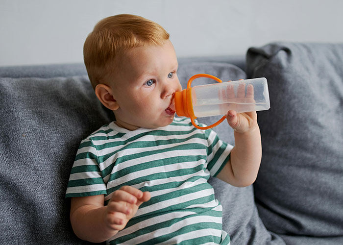 Toddler drinking from a bottle sitting on a couch, illustrating things that are more dangerous than they seem.