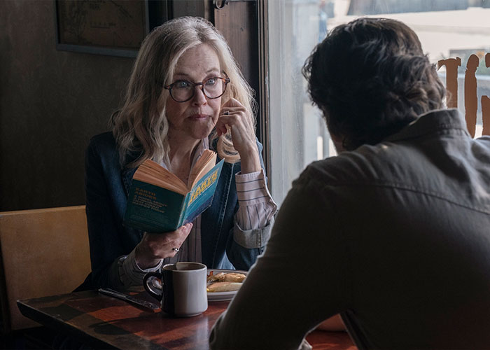 Woman reading a book and talking to a man by the window, relating to Catherine O’Hara’s brother sharing shocking details. Woman reading a book and talking to a man by the window, relating to Catherine O’Hara’s brother sharing shocking details.