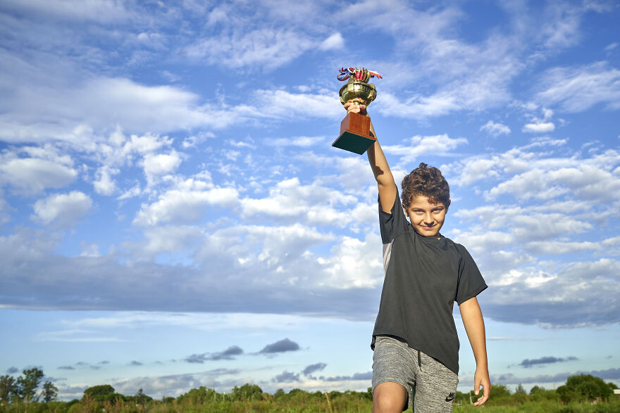 Boy holding a trophy outdoors under blue sky, representing the golden child syndrome and pressure of perfection.