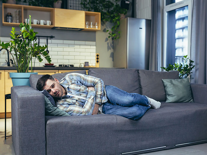 A man lies on a couch, clutching his stomach with a pained expression. He looks sick after a horrible first date.