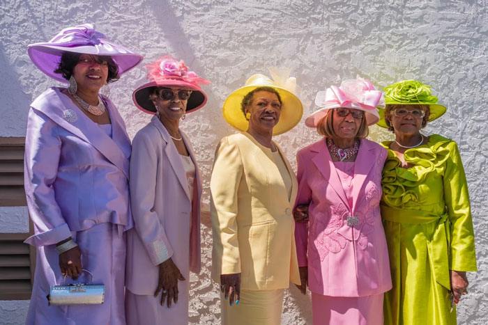 Five elegant Black women wearing colorful church hats and suits, showcasing favorite things.