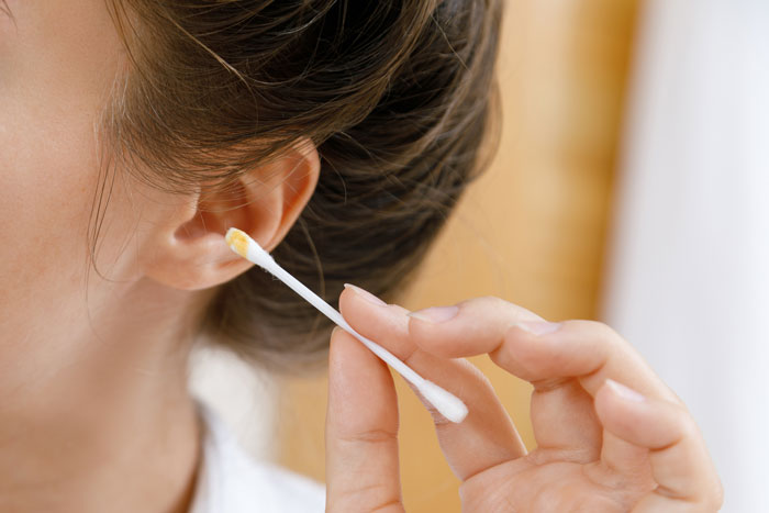 A person cleaning their ear with a cotton swab, showing earwax. This image illustrates gross office stories.