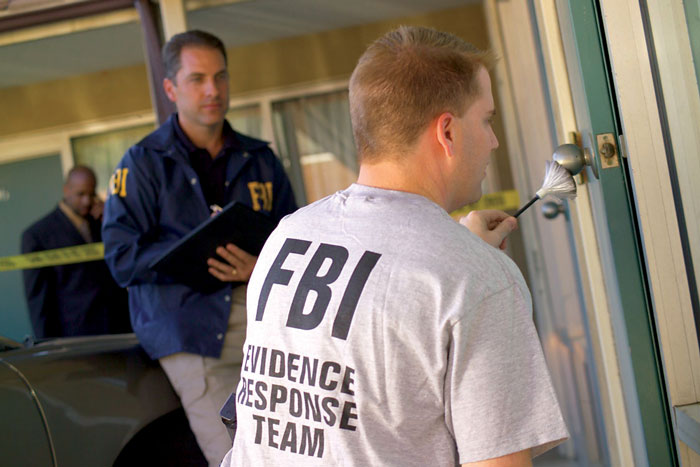 FBI agents investigating a crime scene. One is dusting for fingerprints, revealing something dumb people do.
