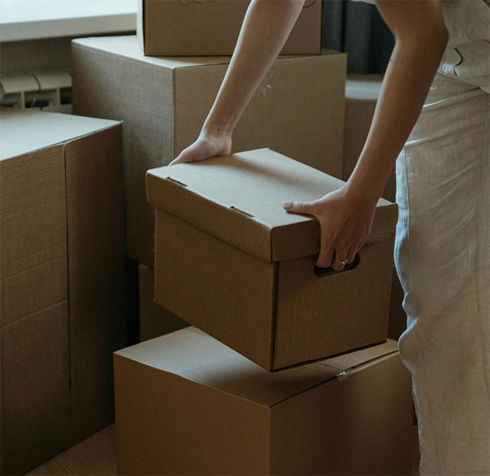 Woman holding a cardboard box among stacked moving boxes, illustrating a story about her mom in a dramatic setting.