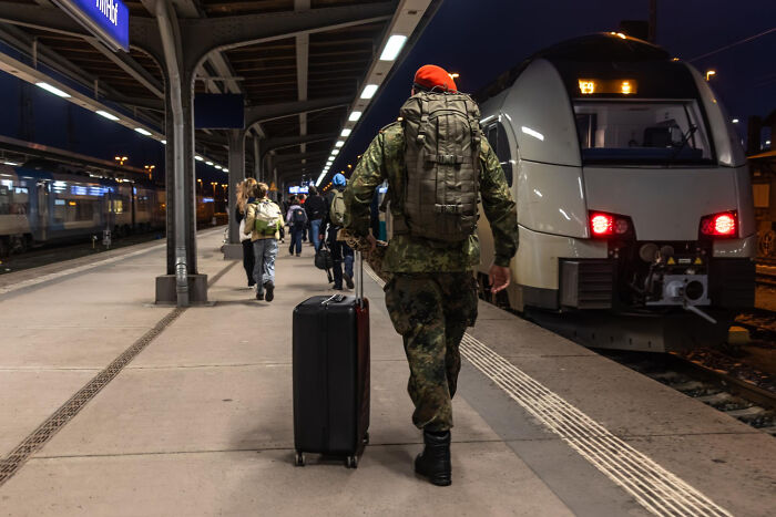 Traveler with large backpack and suitcase walking on platform next to a train, related to TSA confiscated items and travel security.