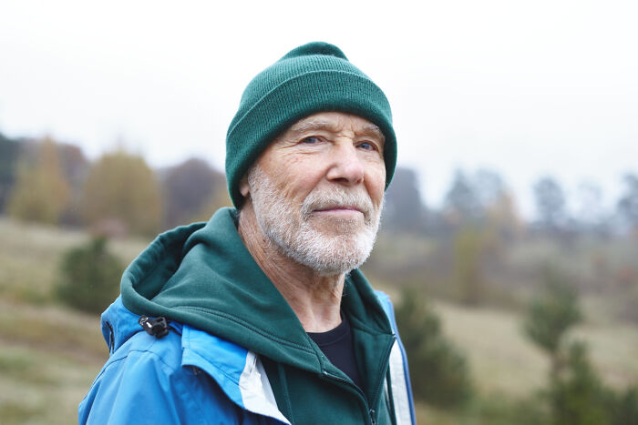 Older man in a green beanie and hoodie, with a blue jacket, looking reflective. He shares celebrity relatives experiences.