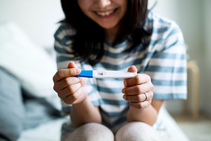 Woman smiling while holding a pregnancy test, illustrating random facts people learned about their bodies at the doctor.