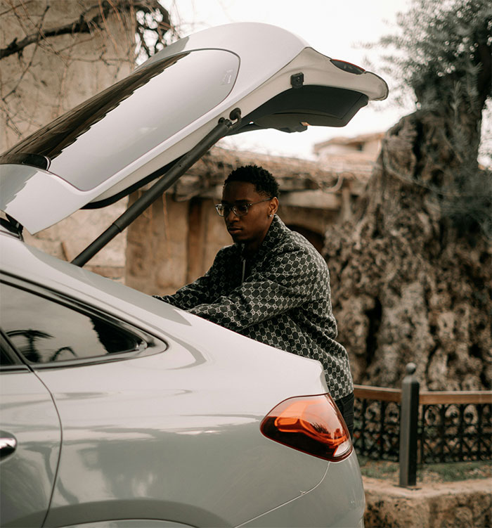 Young man looking serious while standing near car trunk, reflecting on ex-girlfriend cheating incident before wedding event.