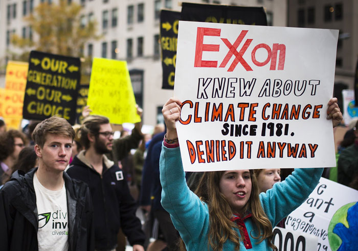 Manifestante segurando cartaz sobre a traição da Exxon na negação das mudanças climáticas durante um grande evento de protesto histórico.