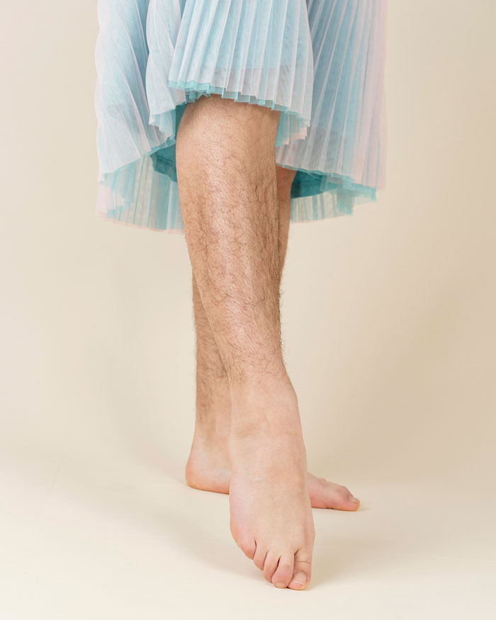 Man wearing a light blue skirt, standing barefoot showing hairy legs, illustrating women making men feel uncomfortable.