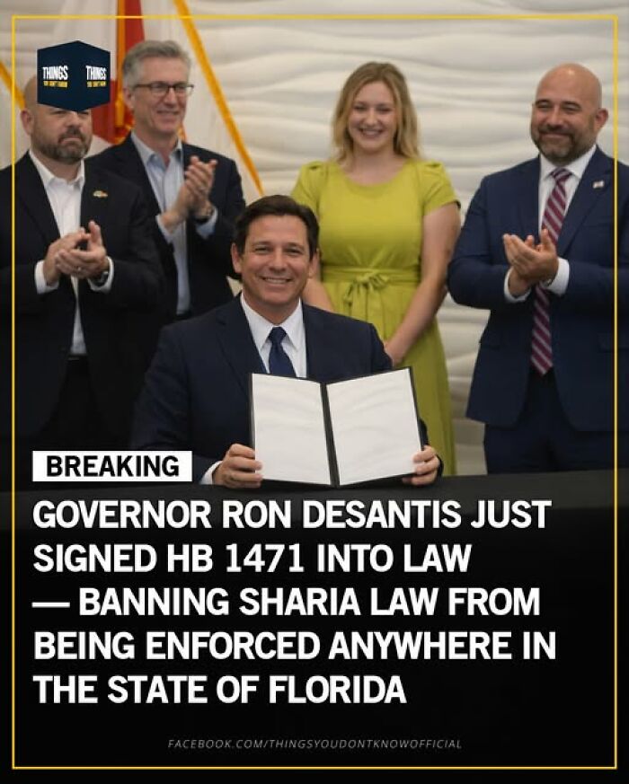 Governor Ron DeSantis signing a law banning Sharia law in Florida, surrounded by applauding officials.