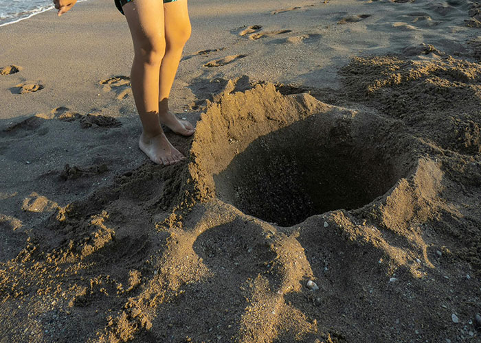 Child standing near a deep sand hole on the beach, showing one of the dangers that are more risky than they seem.