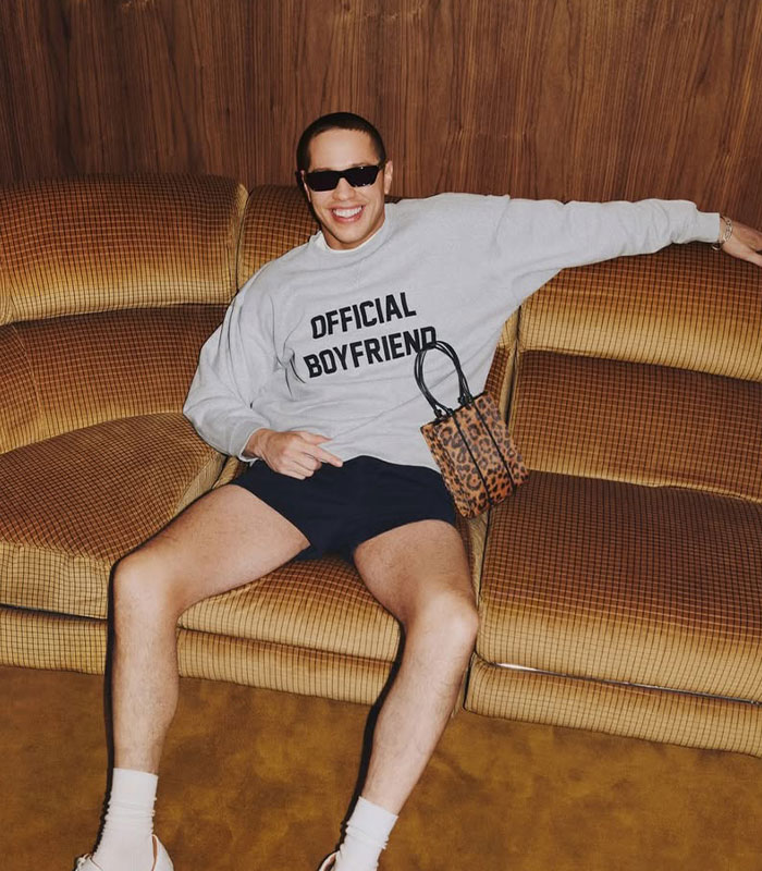 Pete Davidson sitting on a retro couch wearing sunglasses and a sweatshirt, sparking debate about watching adult content.