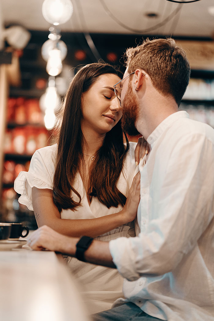 A couple sharing a tender moment, almost kissing, in a warm, dimly lit cafe. Could this be one of those horrible first dates?