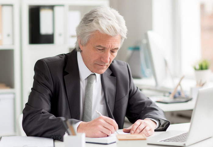 Senior businessman writing at a desk, planning revenge against toxic bosses.